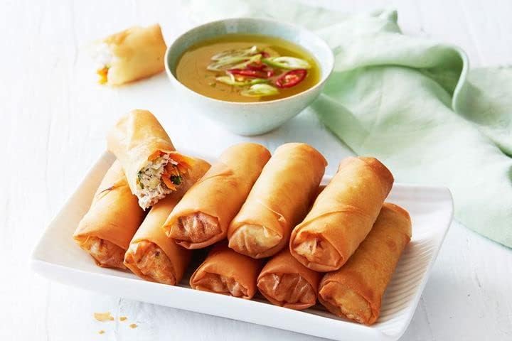 Spring rolls on a plate with a bowl of soup in the background